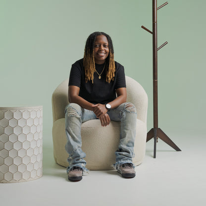 Person wearing a gender-affirming black tee shirt from Bro Code sitting on a beige chair with casual ripped jeans