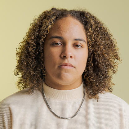 Close-up portrait of a person with curly hair wearing LGBTQIA+ Inclusive Clothing by Bro Code in a light beige top