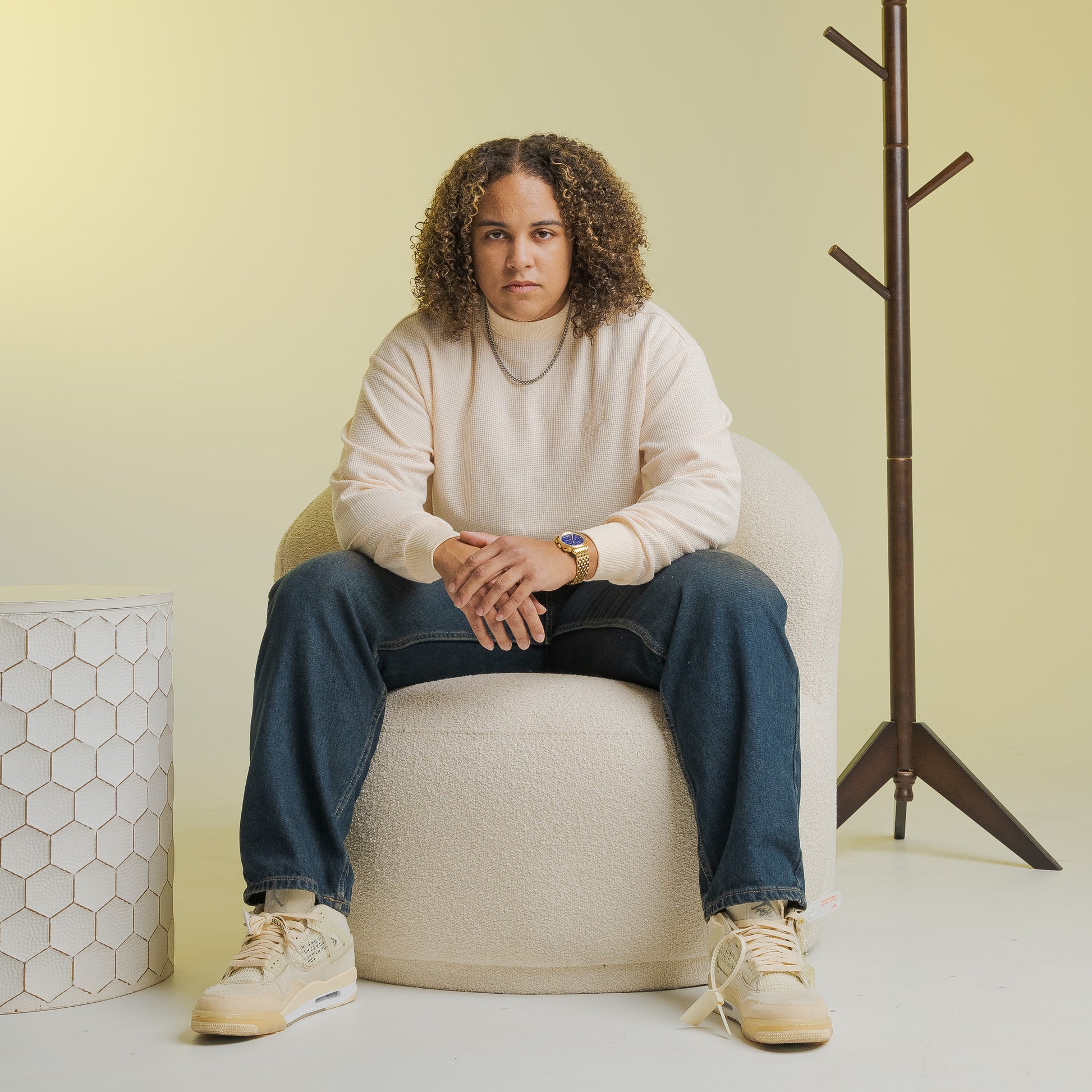 Person wearing Bro Code LGBTQIA+ Inclusive Clothing cream sweatshirt and blue jeans sitting on a white chair