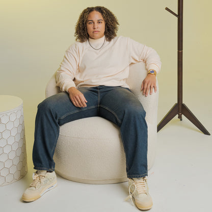 Person wearing Bro Code LGBTQIA+ Inclusive Clothing white sweatshirt and dark jeans seated on a beige chair